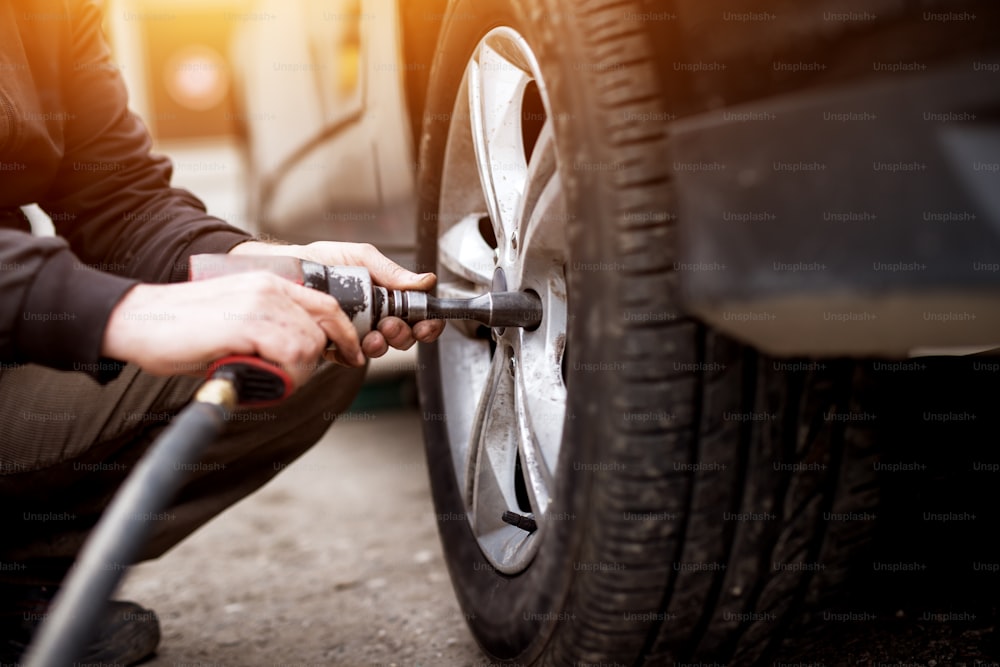 Automechaniker Mann mit Elektroschrauber Reifenwechsel draußen. Autoservice. Hände ersetzen Reifen auf Rädern. Konzept der Reifenmontage.