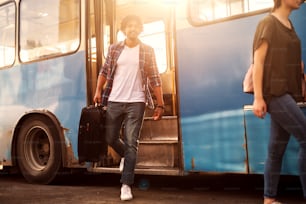 若いハンサムな男が旅行バッグを持ってバスを降りている。