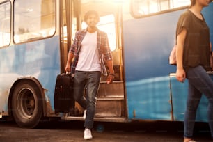 Young handsome man is leaving the bus with his traveling bag.