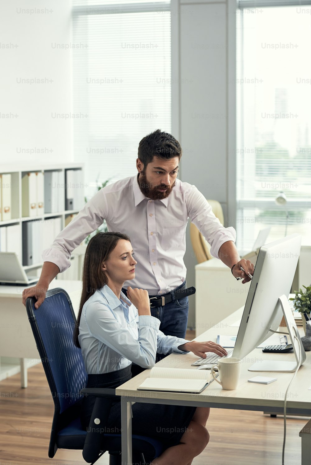 Formal man and woman gathering at table in office and watching computer while talking about new strategy