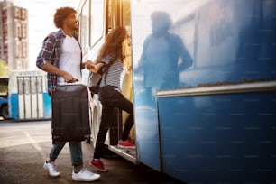 Una joven pareja está entrando en el autobús azul mientras se toma de la mano y un hombre lleva una bolsa de viaje.