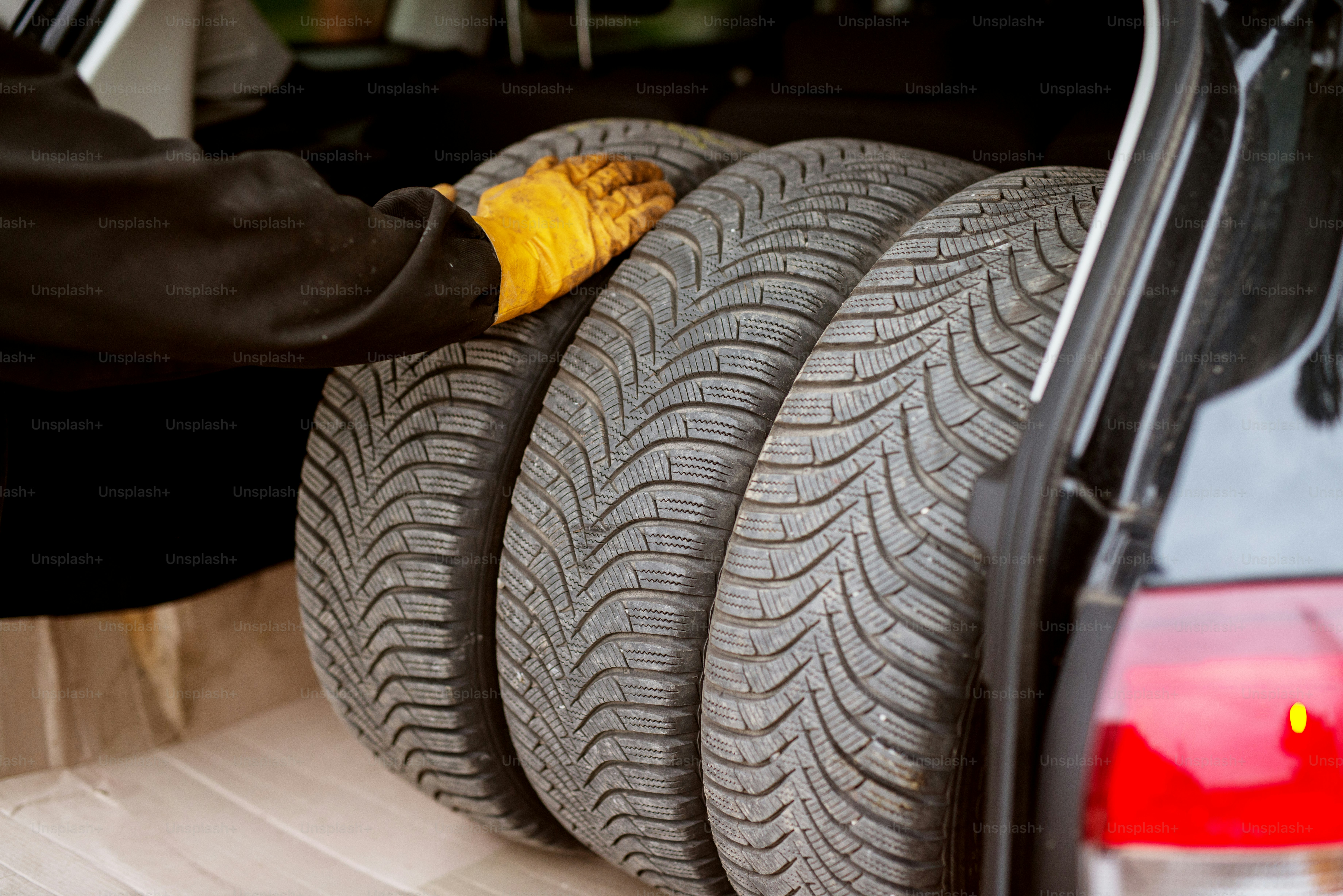 Mecânico trabalhador com luvas laranjas está colocando rodas de carro no porta-malas do carro com cuidado.