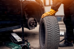 Auto mechanic man with electric screwdriver changing tire outside. Car service. Hands replace tires on wheels. Tire installation concept.