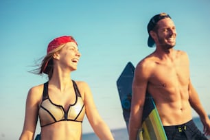 かなり笑顔の白人女性カイトサーファーがボーイフレンドと一緒に砂浜で夏を楽しんでいます。