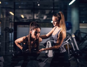 Dos hermosas chicas enfocadas en forma están entrenando juntas en un gimnasio oscuro.