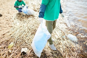 Due esseri umani in uniforme verde con sacchi che puliscono l'area lungo il fiume da vecchie bottiglie di plastica