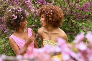 two women standing next to each other in front of purple flowers