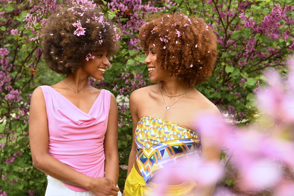 two women standing next to each other in front of flowers