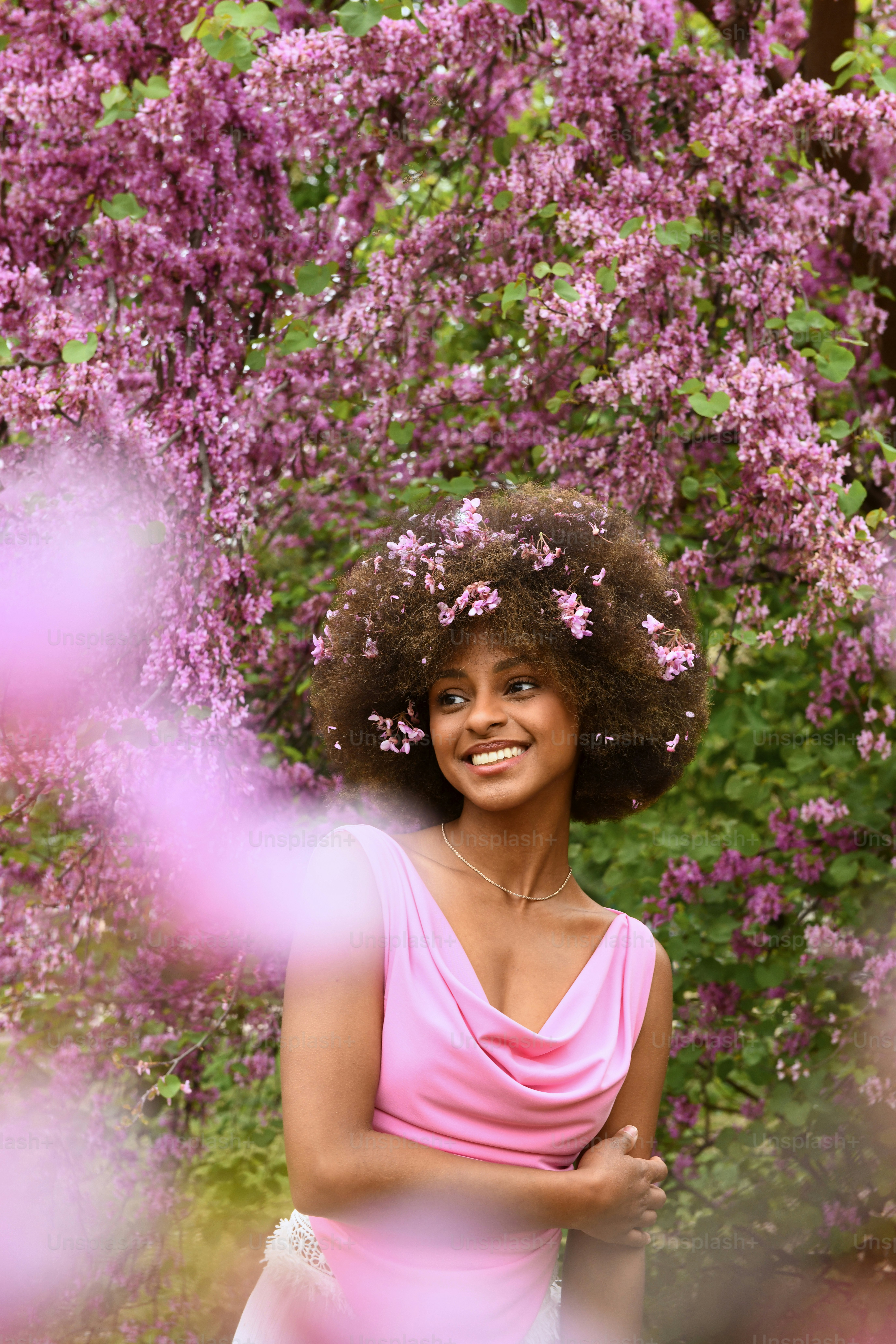a woman in a pink dress standing in front of purple flowers