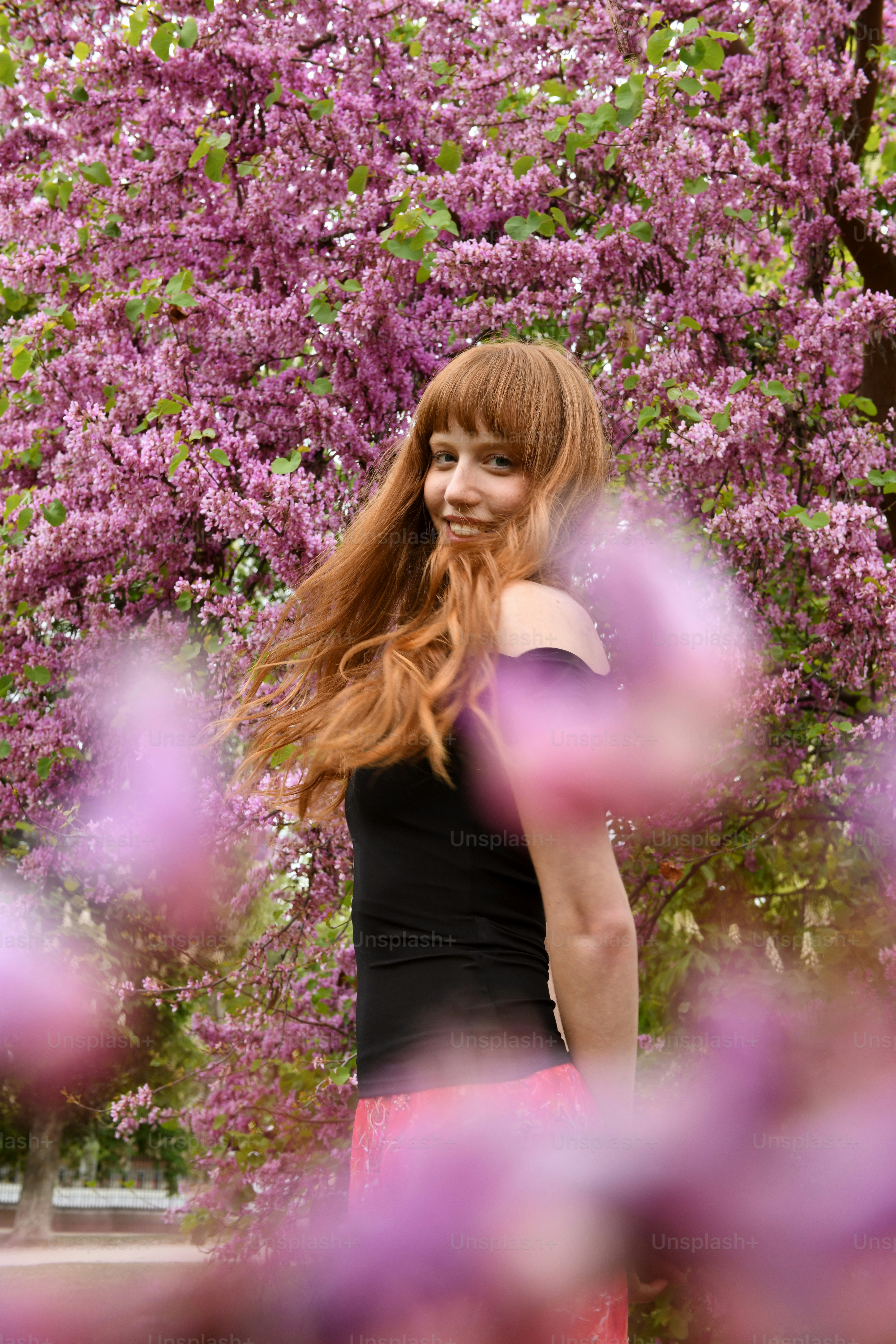 a woman with long red hair standing in front of a tree
