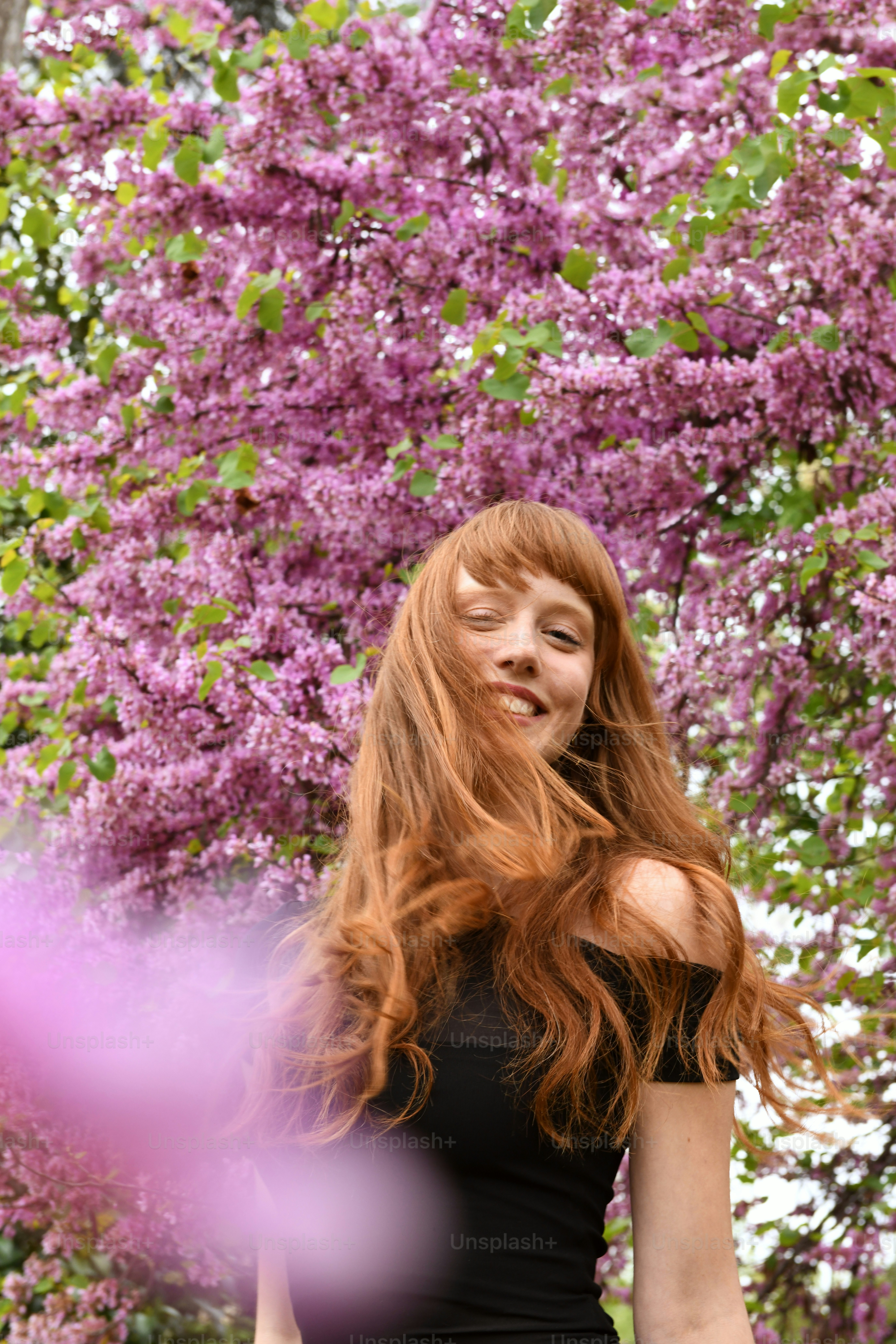 a woman with long red hair standing in front of a tree