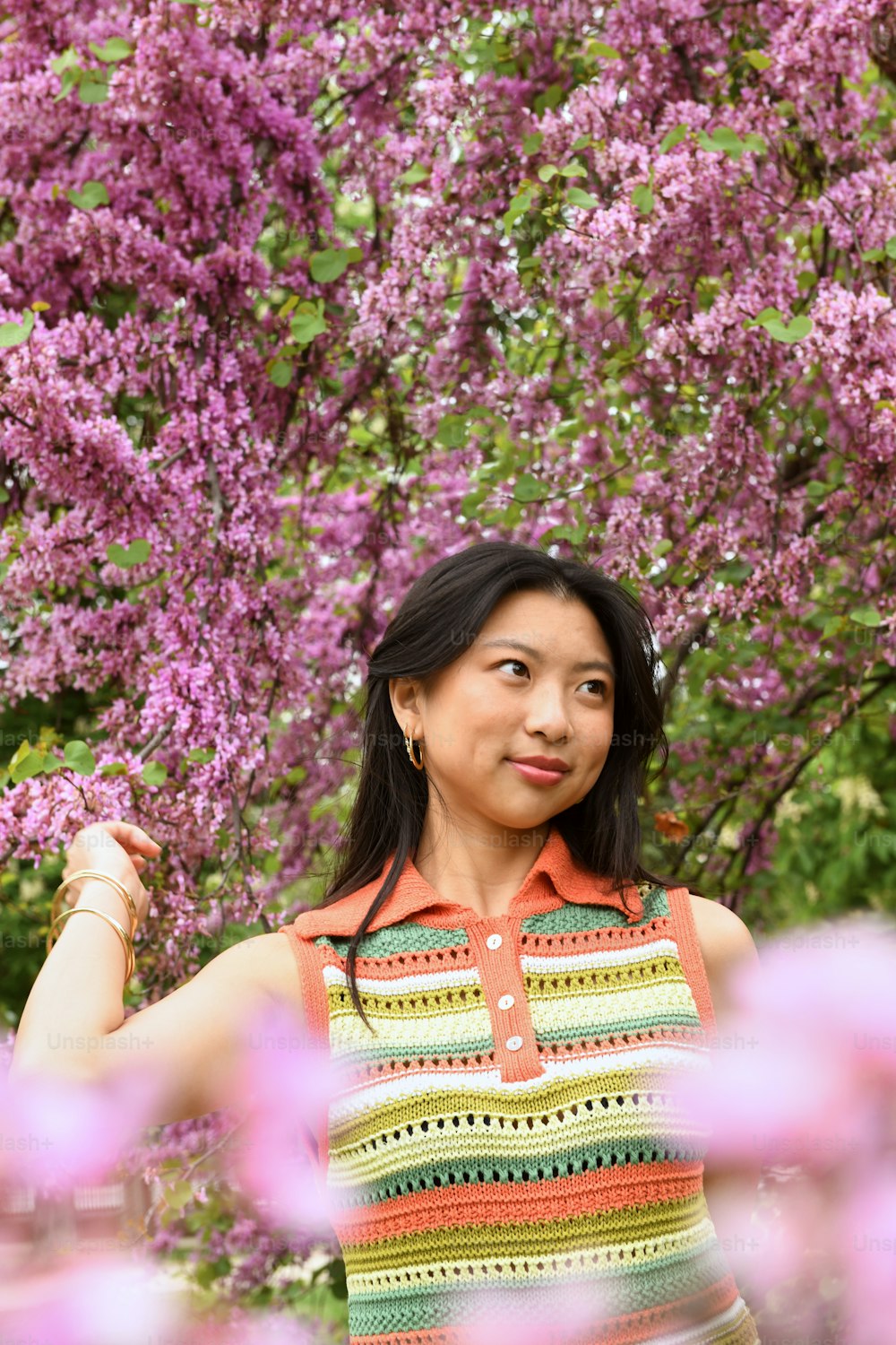 Una mujer parada frente a un árbol con flores púrpuras