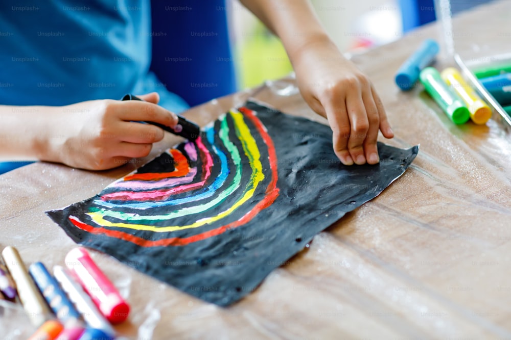 Closeup de criança pintando quadro de arco-íris com cores de vara diferentes no fundo preto durante a pandemia da doença de quarentena do coronavírus. Crianças pintam arco-íris ao redor do mundo