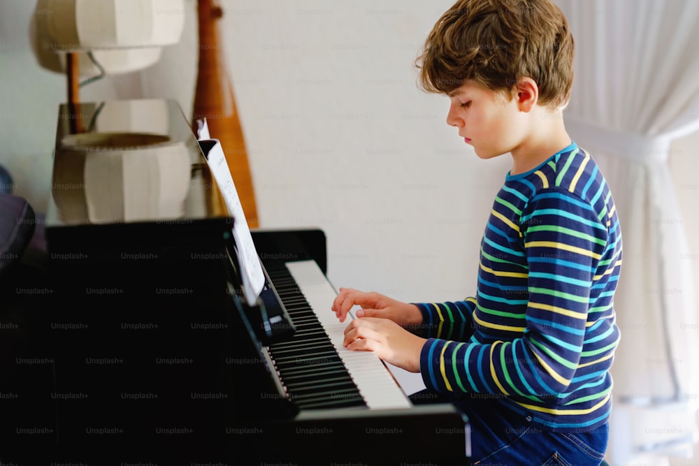 Beautiful little kid boy playing piano in living room. Child having fun with learning to play music instrument with tablet app. E-learning concept during homeschooling corona virus lockdown