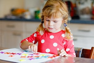 さまざまなカラフルなステッカーで遊んだり、花を描いたりする幼児の女の子。パンデミックコロナウイルス検疫中の子供の活動のコンセプト。家で両親と色を学ぶ子ども。