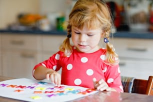 Kleines kleines Mädchen, das mit verschiedenen bunten Aufklebern spielt und Blumen malt. Konzept der Aktivität von Kindern während der pandemischen Quarantäne des Coronavirus. Kind lernt Farben mit den Eltern zu Hause.