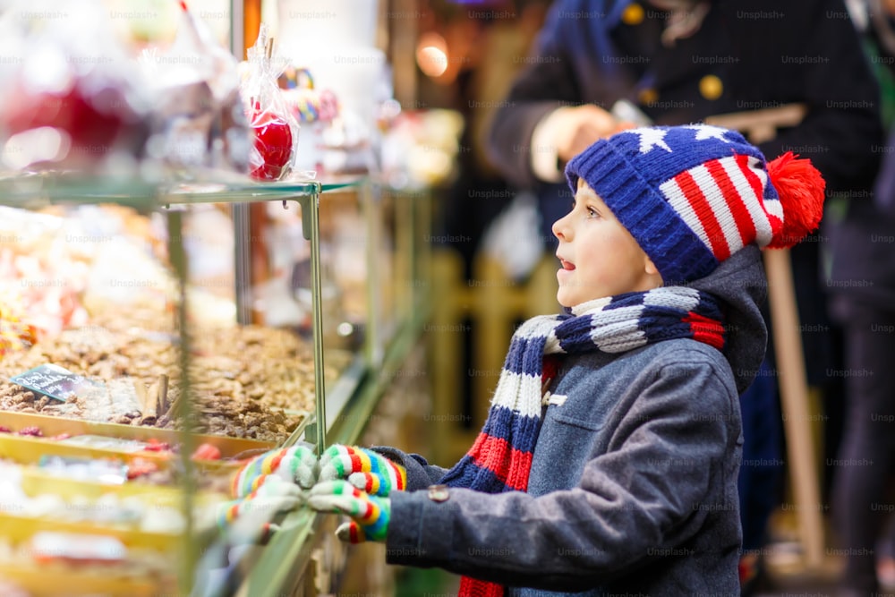 Piccolo ragazzo sveglio vicino a stand dolce con pan di zenzero e noci. Bambino felice sul mercatino di Natale in Germania. Tempo libero tradizionale per famiglie a Natale. Festa, festa, tradizione, infanzia.