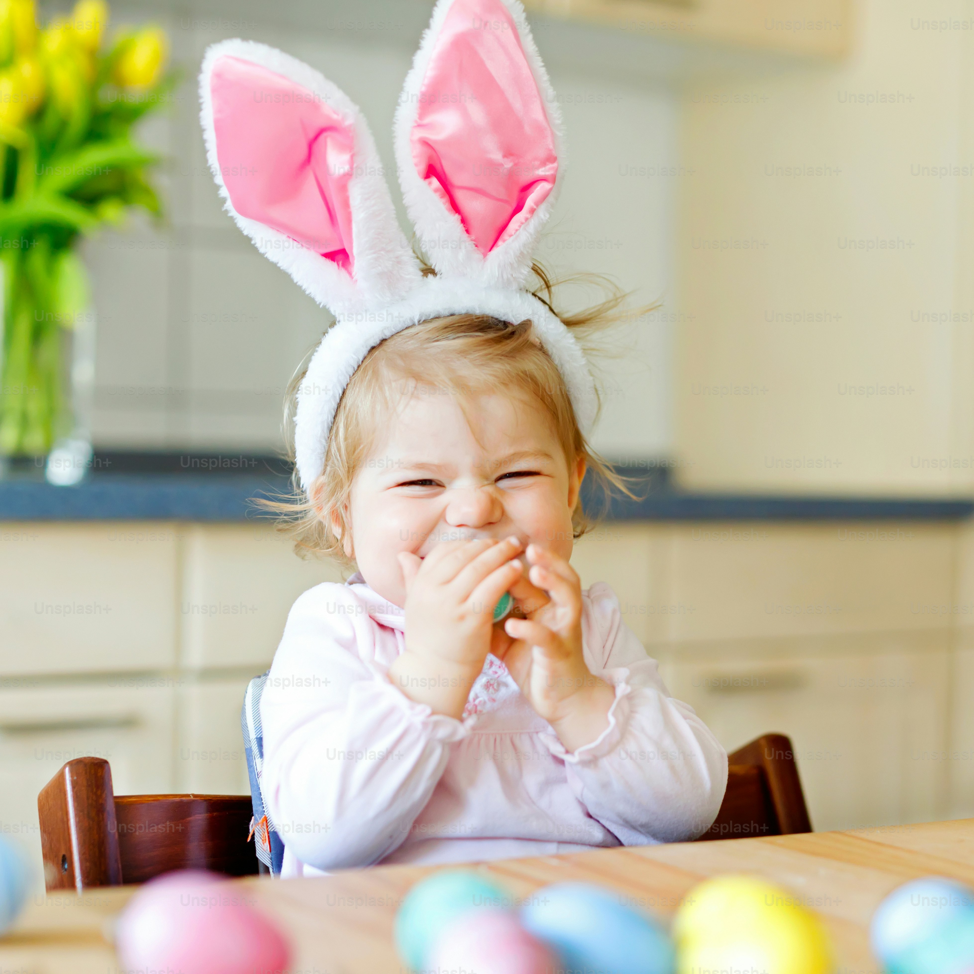 Nettes kleines Kleinkind mit Osterhasenohren, das mit bunten Pastelleiern spielt. Glückliches Baby, das Geschenke auspackt. Entzückendes Kind in rosa Kleidung, das Urlaub genießt.
