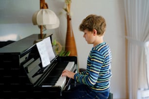 거실에서 피아노를 치는 아름다운 어린 소년. 태블릿 앱으로 악기 연주를 배우는 재미를 느끼는 아이. 홈스쿨링 코로나 바이러스 봉쇄 중 E-러닝 개념