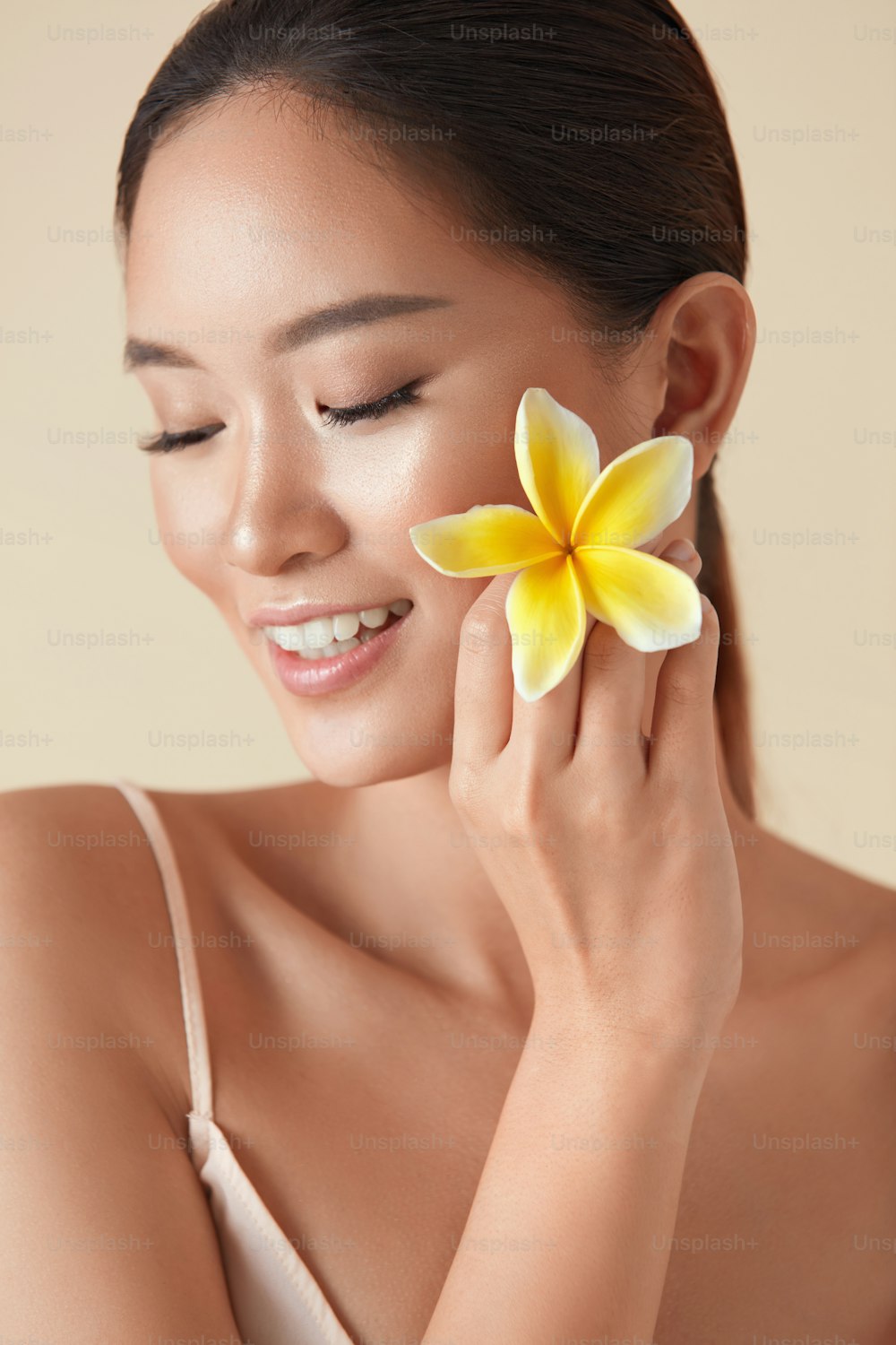 女。美しさと花のポートレート。プルメリアを顔の近くに持つ目を閉じたアジアのモデル。健康的で輝く潤いのある顔の肌と完璧な体のためのスパサロンでの自然療法。