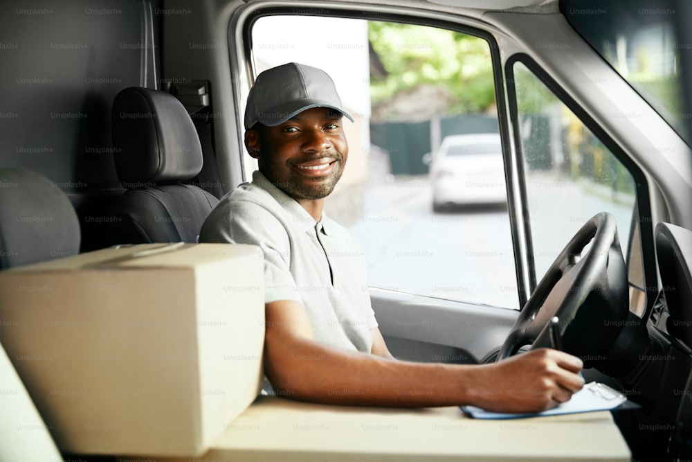 Entrega por Courier. Motorista homem negro dirigindo carro de entrega com caixas e pacotes. Alta Resolução