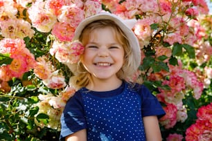 Ritratto della bambina nella fioretta del roseto. Bello bambino carino che si diverte con rose e fiori in un parco in una giornata di sole estivo. Bambino sorridente felice