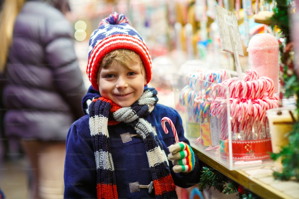 Pequeño niño lindo cerca de dulce puesto con bastones de caramelo. Feliz niño en el mercado navideño en Alemania. Ocio tradicional para familias en Navidad