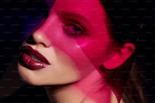 メイクアップビューティー。ピンクの光の下に暗い口紅を持つ女性モデル。美しいセクシーなメイク、リップグロス、カラーライトの下で輝く肌を持つ魅力的な女の子の接写。高画質画像