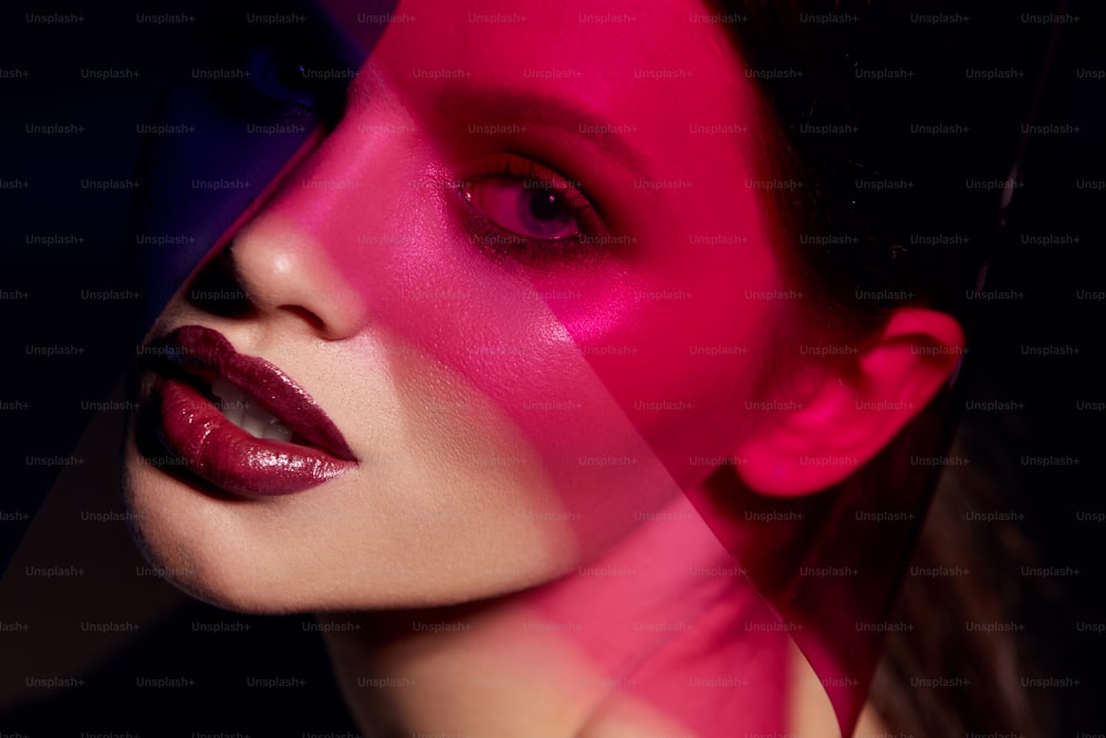 Makeup beauty. Woman model with dark lipstick under pink light. Closeup portrait of glamorous girl with beautiful sexy make-up, lip gloss and glowing skin under color lights. High quality image