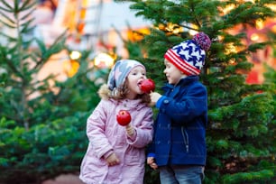 Two little smiling kids, boy and girl hugging on German Christmas market. Happy children in winter clothes with lights on background and xmas trees. Family funny brother and sister