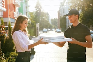 Livraison de pizzas. Courrier donnant des boîtes à femme avec de la nourriture à l’extérieur. Client recevant la commande. Haute résolution