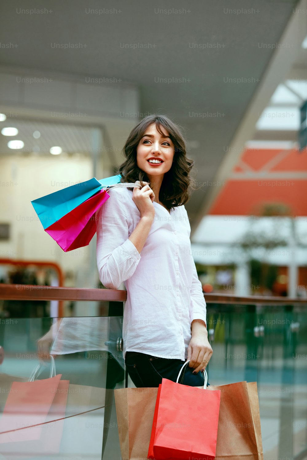 Mujer en centro comercial, mujer con bolsas de colores divirtiéndose en centro comercial. Alta resolución.