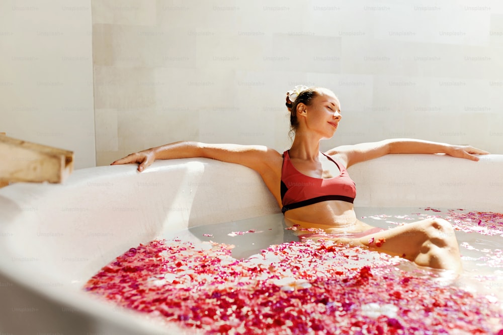 Woman In Bath At Day Spa Salon. Beautiful Smiling Girl In Bikini Bathing, Bathe With Flower Petals In Summer. Sexy Female Relaxing Outdoors. Aroma Therapy Beauty Treatment, Body Care. Relax Concept