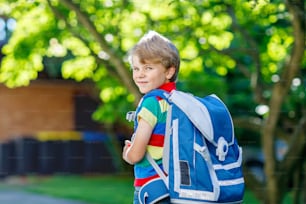Happy little kid boy in colorful shirt and backpack or satchel on his first day to school or nursery. Child outdoors on warm sunny day, Back to school concept. Boy in colorful uniform