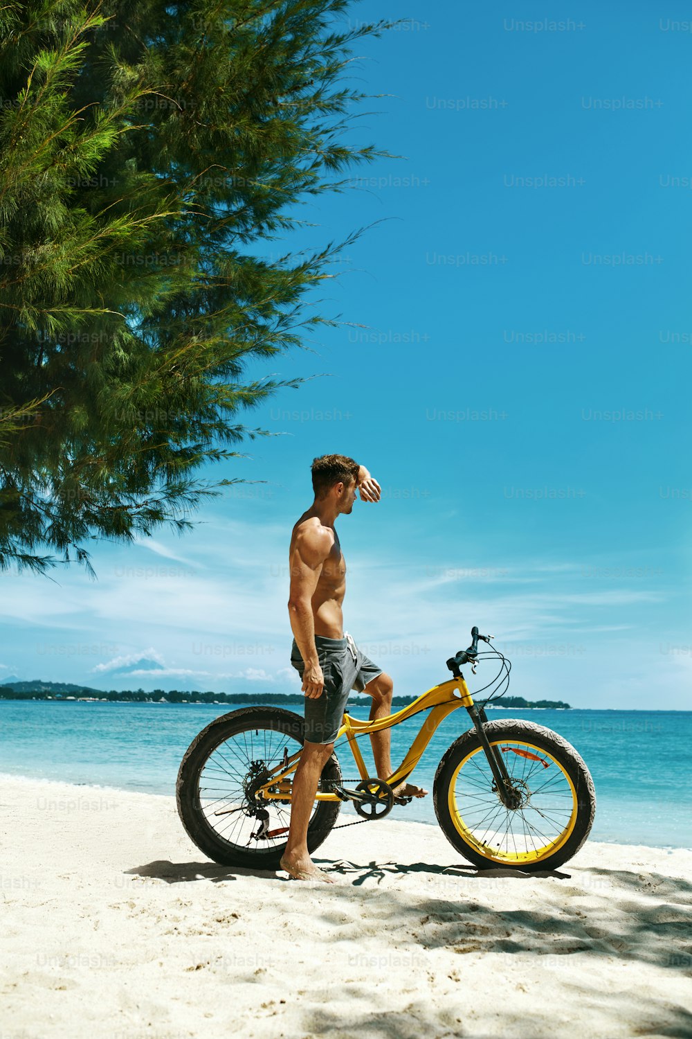 여름 해변 스포츠. 근육질의 몸매를 가진 운동선수가 열대 해변에서 노란 모래 자전거를 타고 있다. 휴가 여행 휴가에 자전거를 탄 피트니스 남성 모델. 스포츠 활동, 활동적인 라이프스타일 개념
