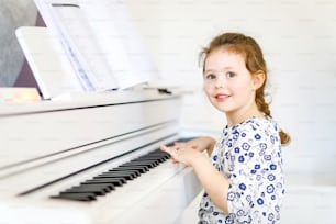 거실이나 음악 학교에서 피아노를 연주하는 아름다운 어린 소녀. 미취학 아동이 악기 연주를 배우는 재미를 느낍니다. 교육, 기술 개념.
