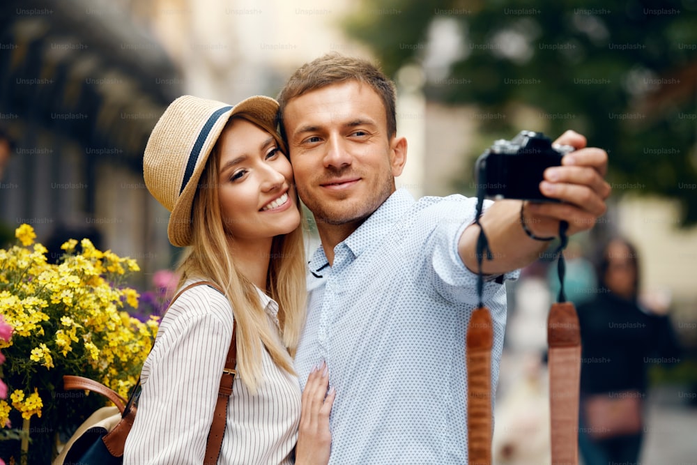 Hermosa pareja tomando fotos con cámara en la calle. Personas sonrientes felices tomando fotos selfie al aire libre mientras viajan juntos. Alta resolución.