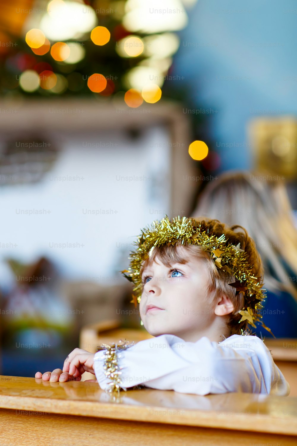 Beautiful little kid boy as an angel in Christmas story in a church. Happy adorable blond child with lights and xmas tree on background.