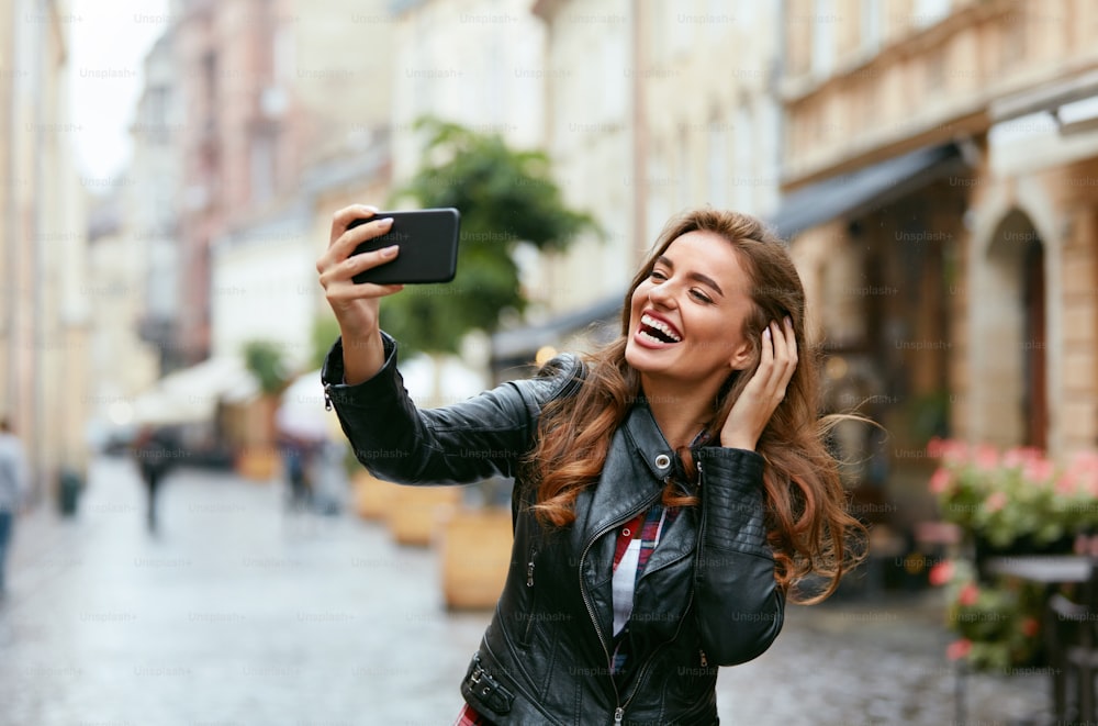 Woman Video Calling On Phone On Street. Smiling Young Female Taking Photos On Mobile Phone Outdoors. High Resolution