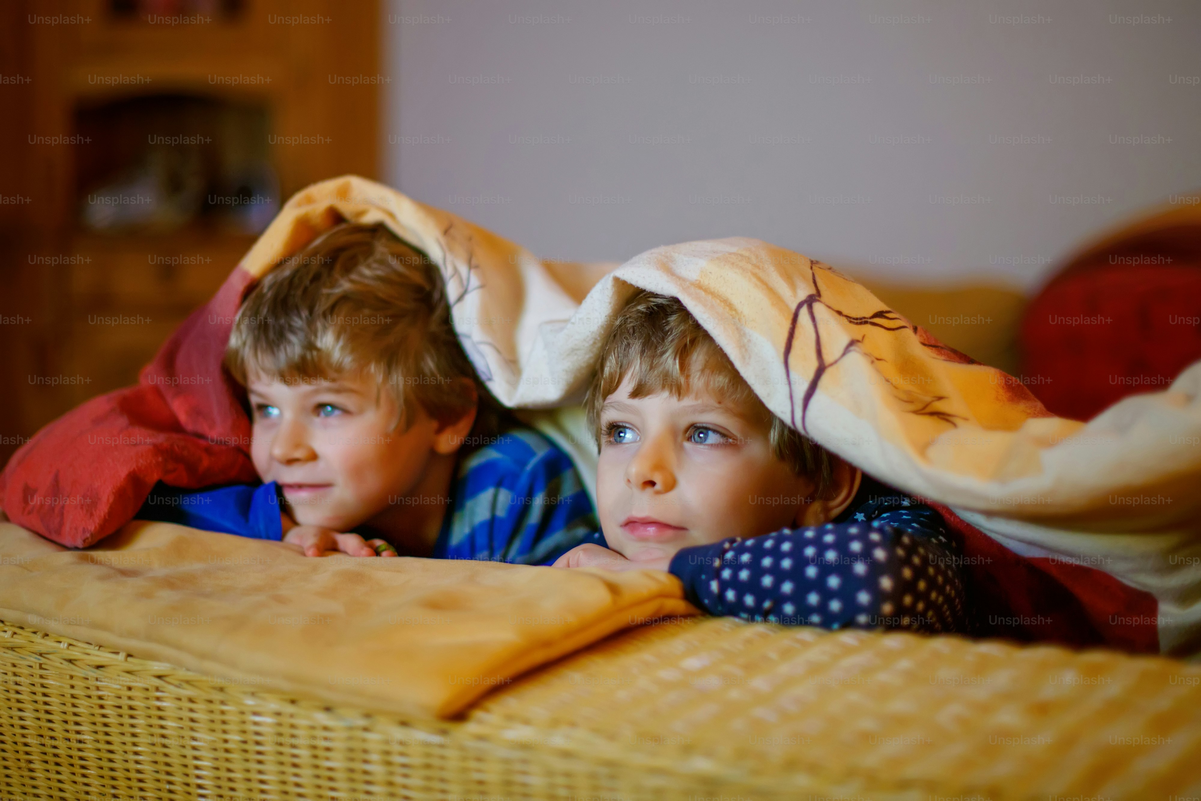 Happy little brothers, adorable kid boys watching television while lying. Funny children enjoying cartoons