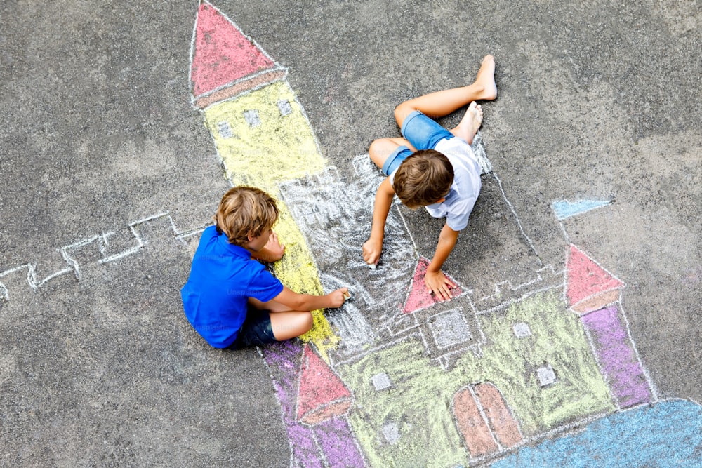 Duas crianças meninos desenhando castelo cavaleiro com giz colorido no asfalto. Irmãos e amigos felizes se divertindo com a criação de quadros a giz e pintura. Lazer criativo para crianças no verão