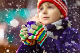 Petit garçon mignon avec une tasse de chocolat chaud fumant ou un punch pour enfants. Enfant heureux sur le marché de Noël en Allemagne. Loisirs traditionnels pour les familles à Noël
