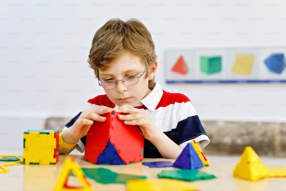 Little kid boy with glasses playing with lolorful plastic elements kit in school or preschool nursery. Happy child building and creating geometric figures, learning mathematics and geometry