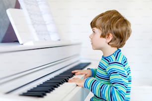 Beautiful little kid boy playing piano in living room or music school. Preschool child having fun with learning to play music instrument. Education, skills concept.