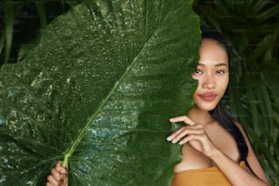 피부 관리. 아름다운 얼굴과 천연 녹색 잎 식물을 가진 여성 모델. 열대 자연에서 누드 손톱과 섹시한 미소를 가진 아름다운 아시아 소녀의 초상화