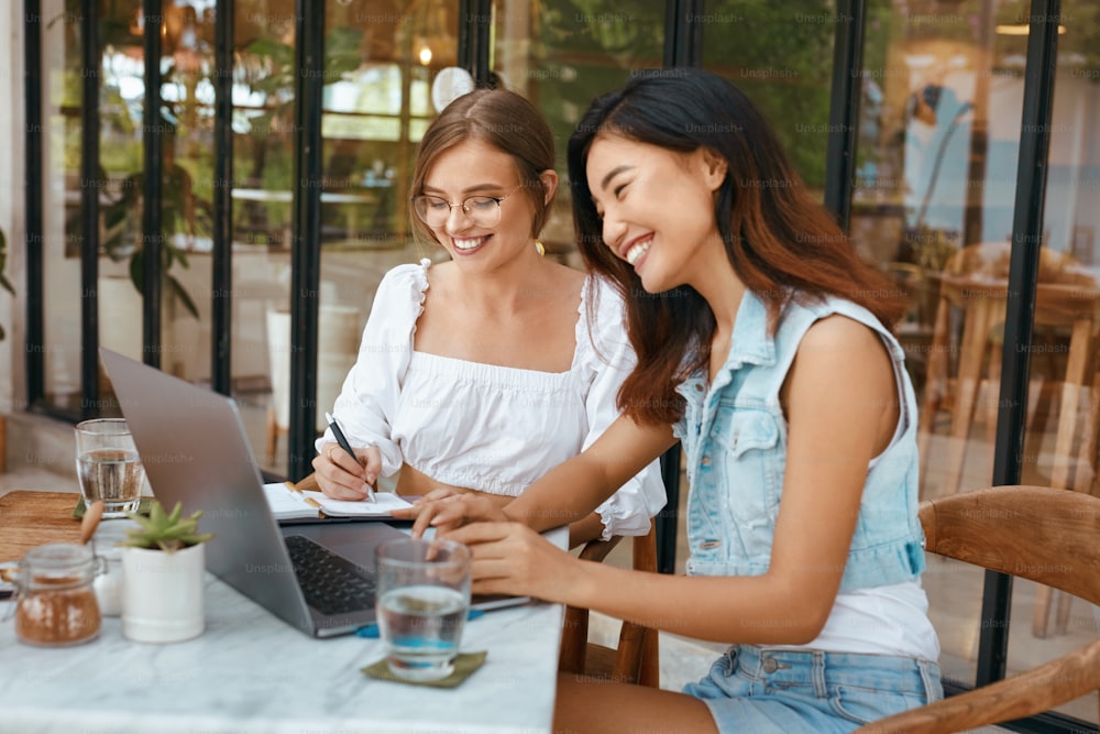Girls Working At  Coffee Shop. Women With Laptop Having Meeting At Cafe. Beautiful Colleagues In Casual Clothes Using Modern Technologies For Communication And Supporting Business.