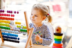 Entzückendes niedliches schönes kleines Kleinkindmädchen, das mit einer pädagogischen hölzernen Regenbogen-Spielzeugpyramide und einem Gegenabakus spielt. Gesundes, glückliches Baby, das Zählen und Farben lernt, drinnen an einem sonnigen Tag
