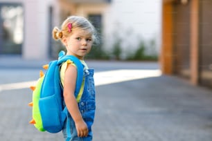 Cute little adorable toddler girl on her first day going to playschool. Healthy beautiful baby walking to nursery school and kindergarten. Happy child with backpack on the city street, outdoors