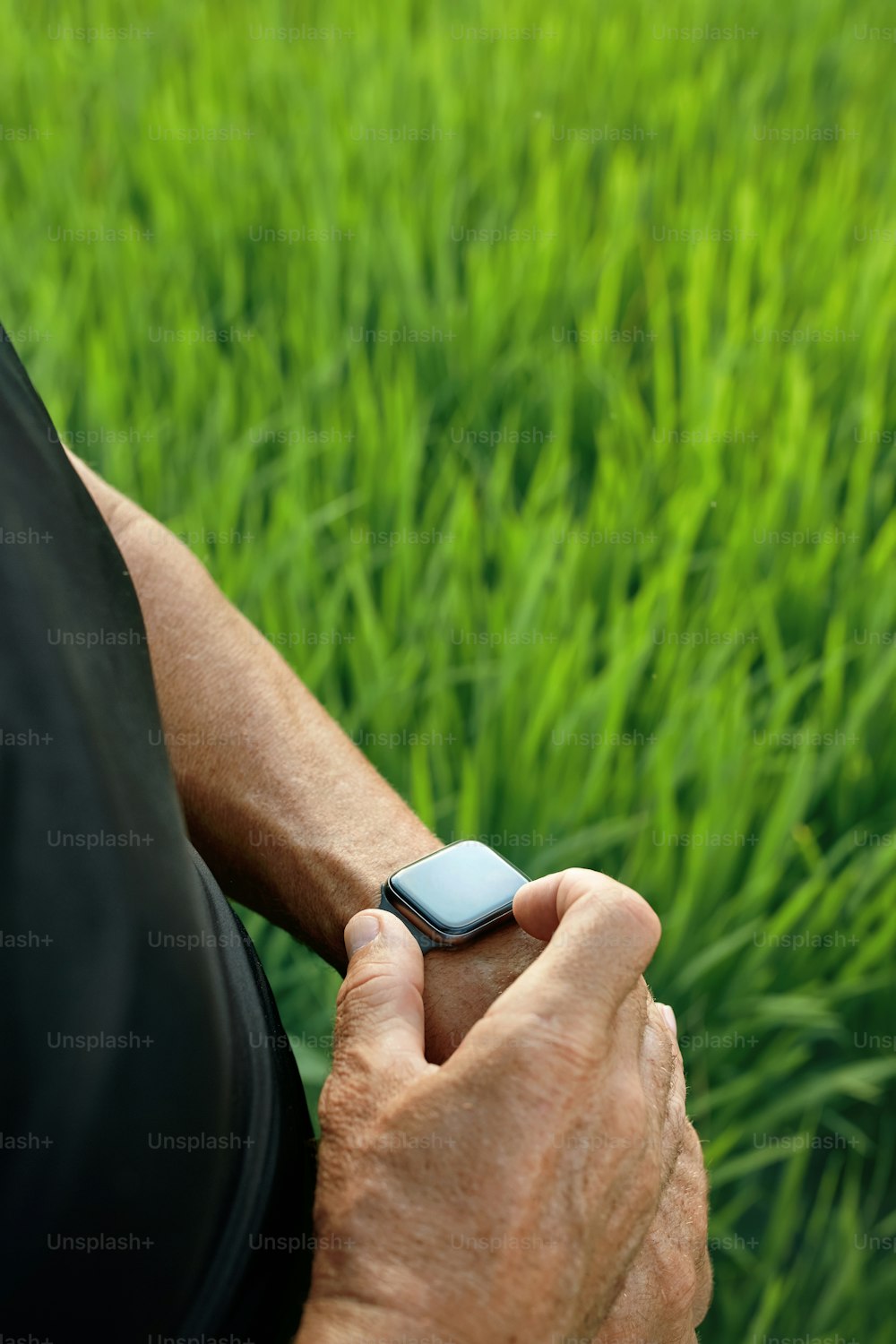 야외에서 운동을 한 후 스마트 시계를 확인하는 스포티한 남자. 논밭의 푸른 잔디에 손목에 피트니스 트래커를 착용한 남성의 손을 닫습니다.