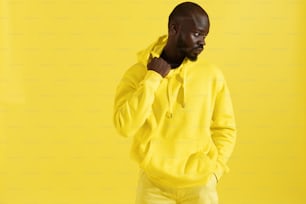 Fashion portrait of black man in yellow hoodie on color background. Handsome african american male model in stylish sweatshirt with hood posing in studio